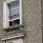 A child looks down from their flat through a window