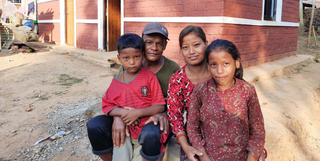 a family sit together outside their new house