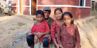 a family sit together outside their new house