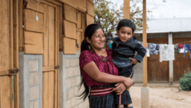 a MOTHER HOLDS HER SON OUTSIDE hABITAT FOR hUMANITY HOMES