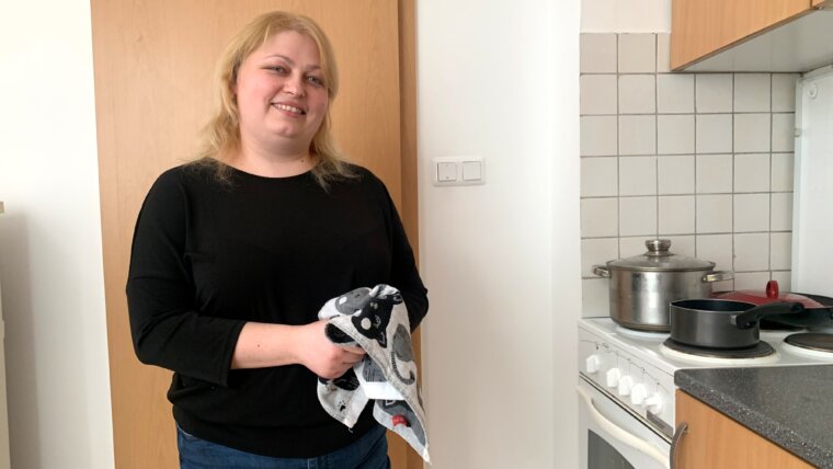 Valentina stands by the stove with a tea towel in her new accommodation in Hungary - Ukraine refugee.