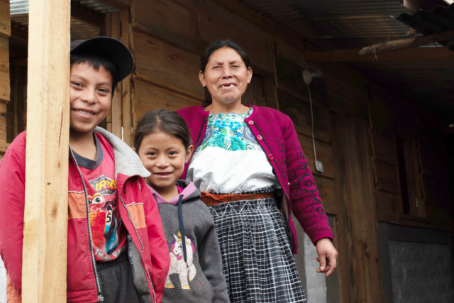 Maria and two of her children stand on the porch of their new home in Guatemala.