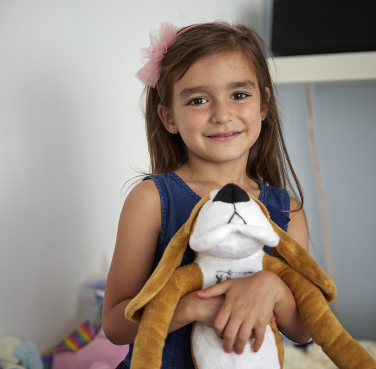 Kira, 6 year old child from Mariupol, Ukraine, smiling whist holding a soft toy animal