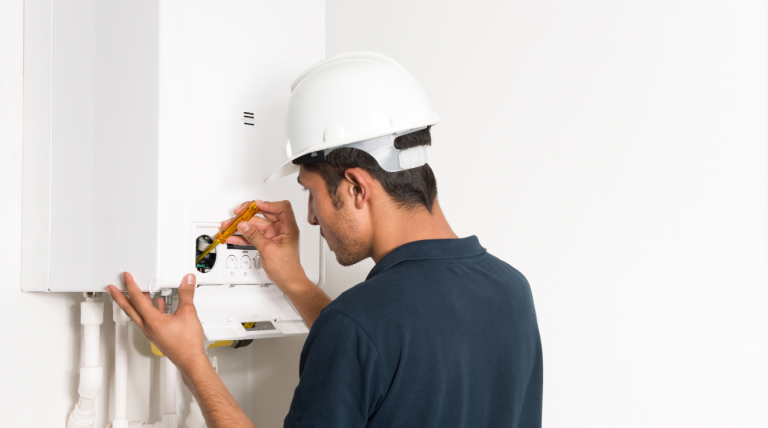 A person in a white hard hat and black t-shirt fixing a boiler.