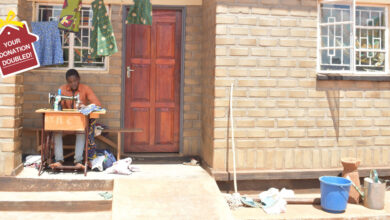 Imraan Chisanga an 18 year old tailor trained by Habitat for Humanity Malawi after Cyclone Freddy, sat outside of his new Habitat for Humanity home, using a sewing machine to tailor clothing