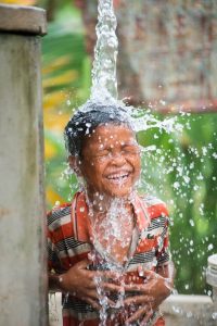 A young boy stands under clean, flowing water in Cambodia