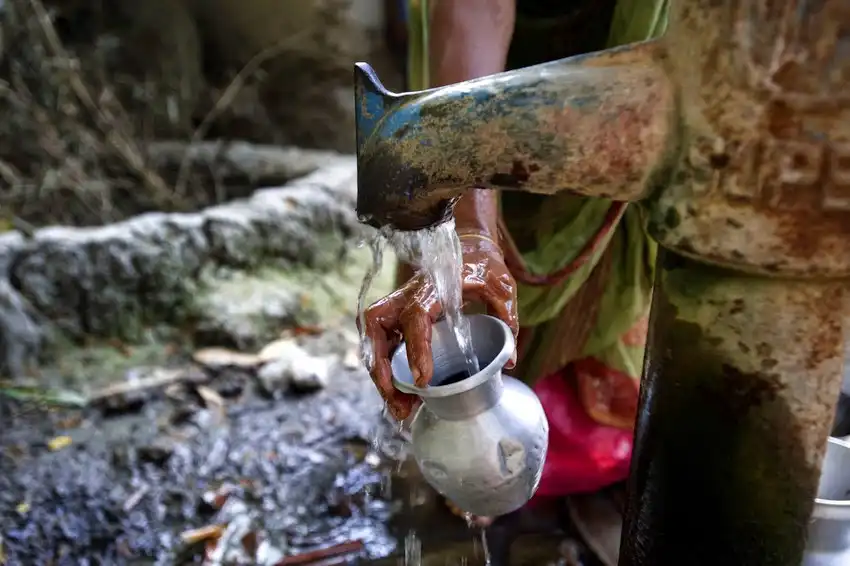 A person collecting water in a metal cup from a tap
