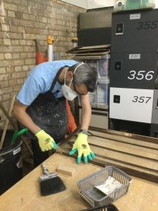 A volunteer in a mask and gloves refinishing furniture at a Habitat ReStore upcycling workshop