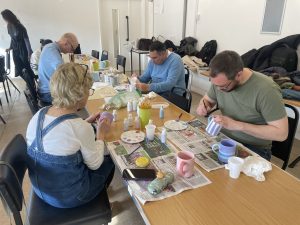 Volunteers painting mugs and ceramics around a table at a Habitat craft workshop