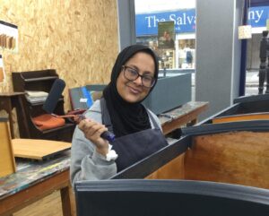 A smiling volunteer in an apron painting furniture at a Habitat ReStore upcycling workshop