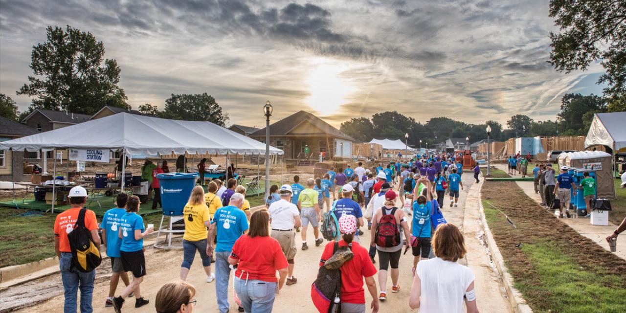 Crowd of volunteers walking together towards a Habitat build site at sunset