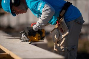 Volunteer in a blue Habitat for Humanity helmet working on a construction site