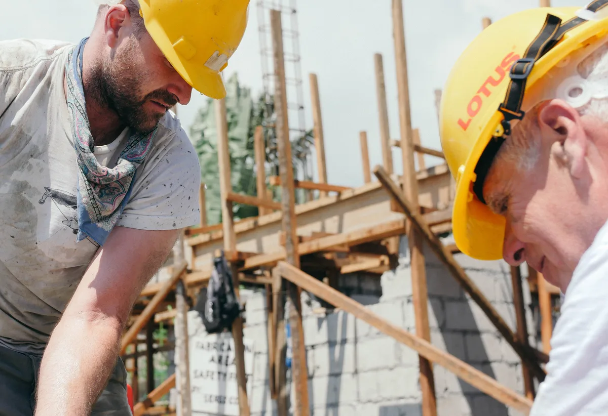 Two people in hard hats building a timber frame