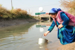 A single mother collecting water from a river in a community without clean water