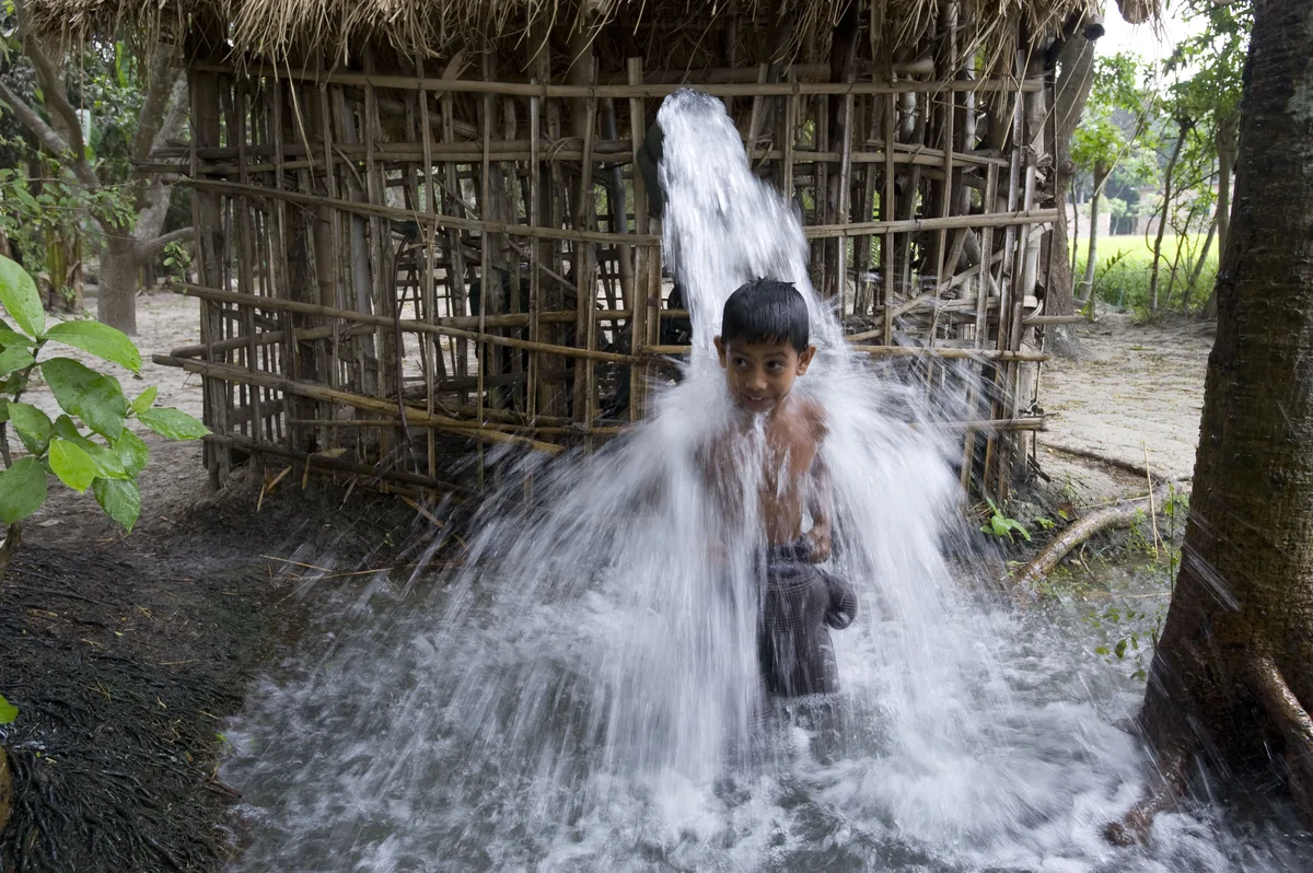 Water gushing from a pipe onto a small smiling boy