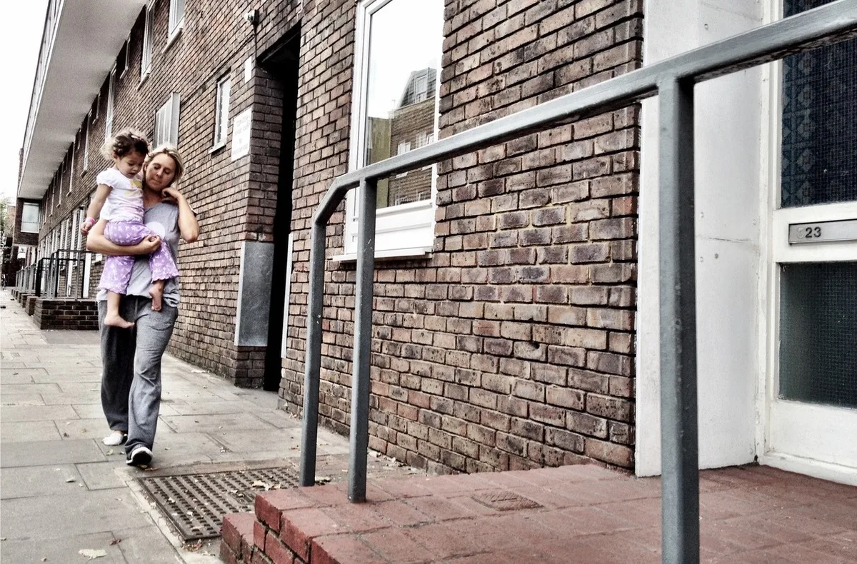 Woman holding her child walking to their front door on a UK housing estate