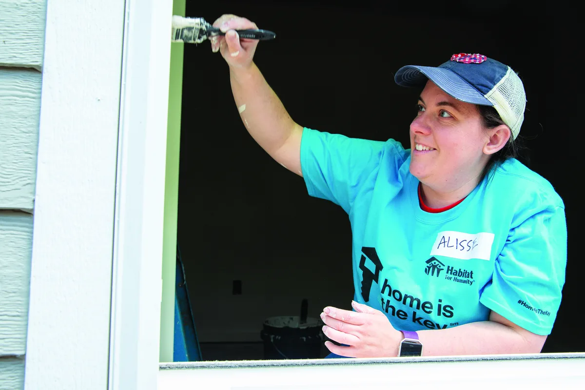 A Habitat volunteer in a branded T-shirt painting a wall