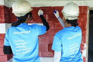 Volunteers in hard hats building a brick wall together