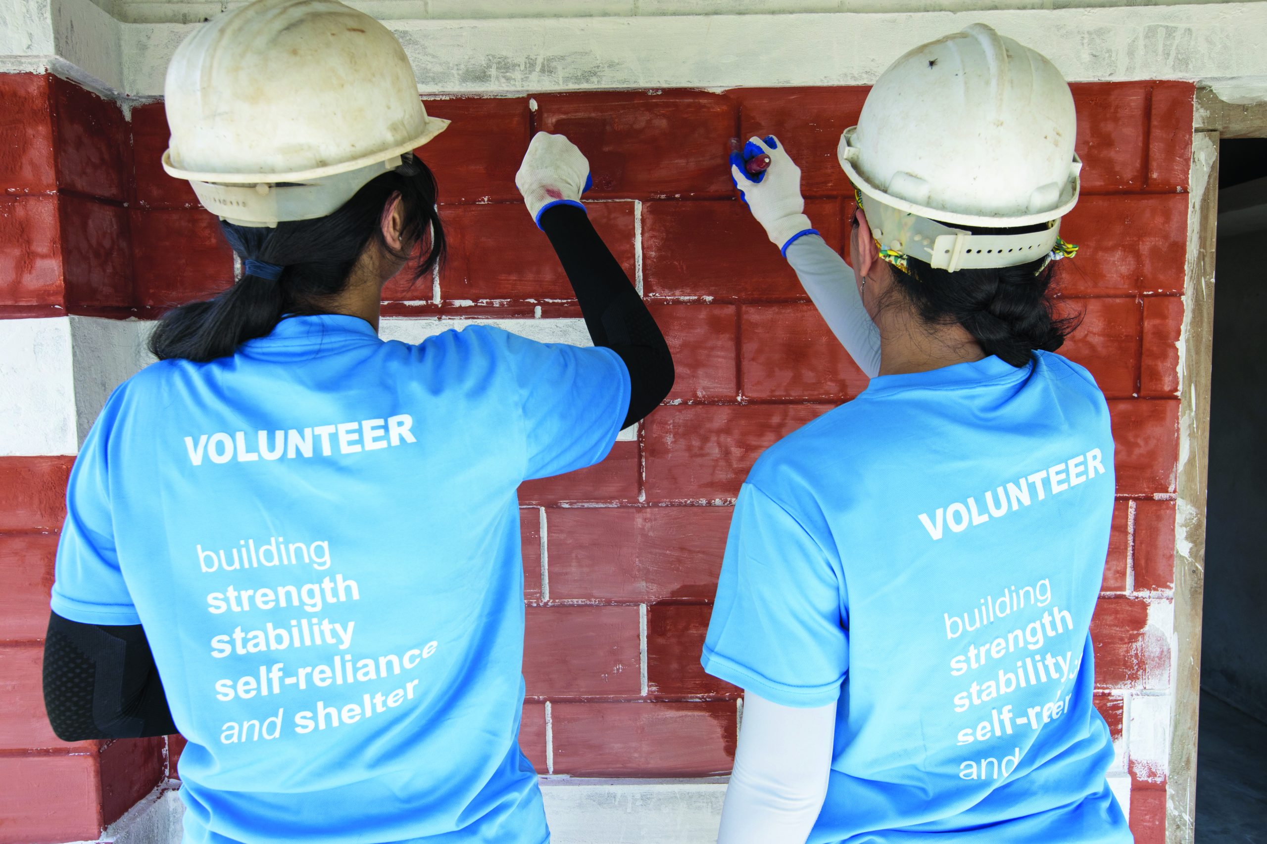 Volunteers in hard hats building a brick wall together